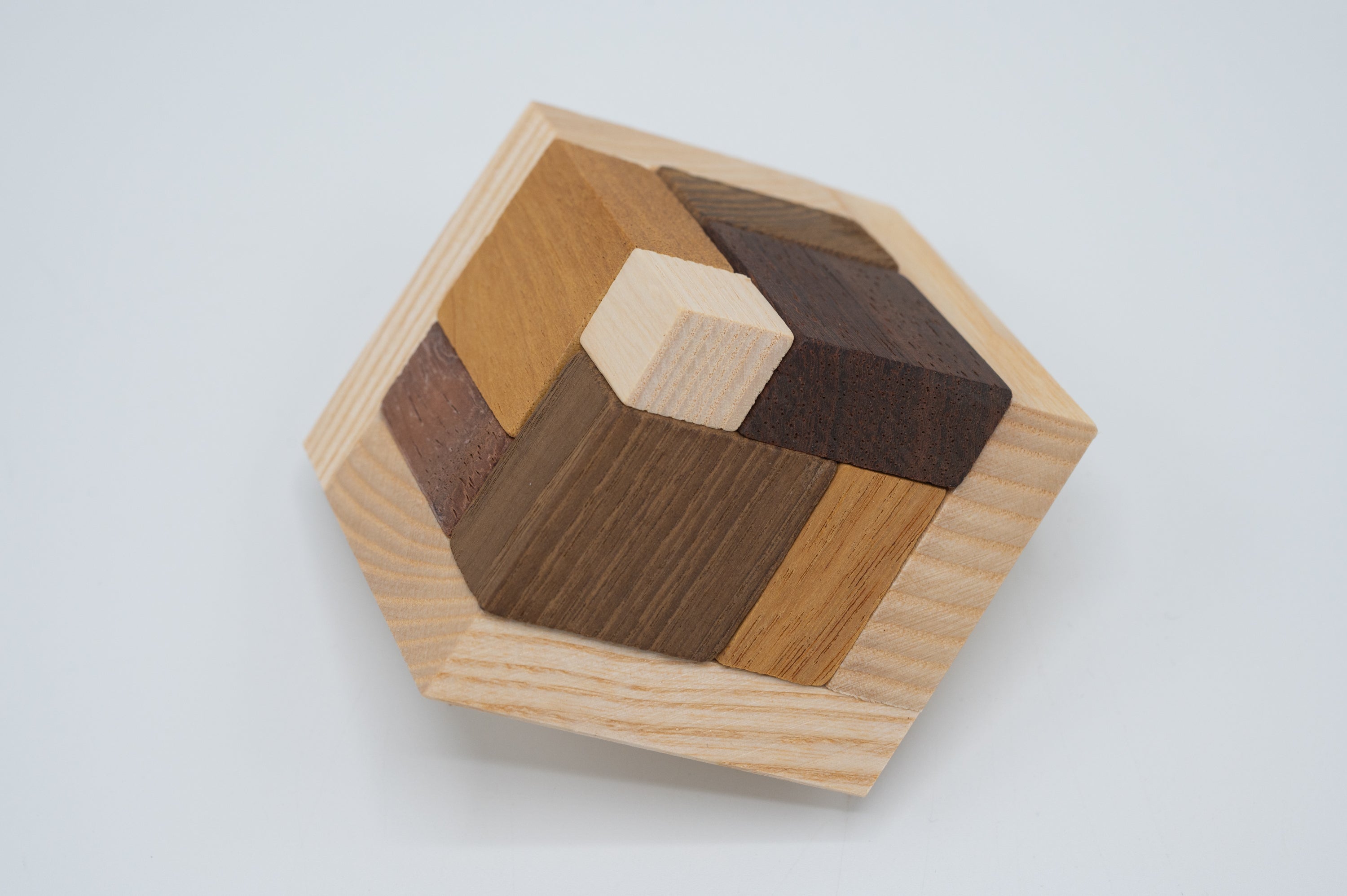 Perspectiv 2 mini mechanical puzzle by Jean Claude, featuring interlocking wooden pieces in varying shades. The hexagonal design includes rich textures and colors, providing a challenging and engaging experience for puzzle enthusiasts.