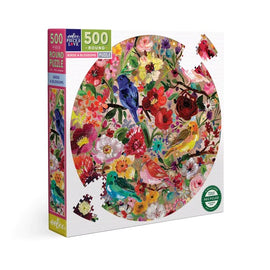Eeboo Birds & Blossoms 500-piece round jigsaw puzzle featuring a vibrant illustration of colorful birds and assorted flowers, displayed in a colorful box. The puzzle promotes creativity and relaxation.