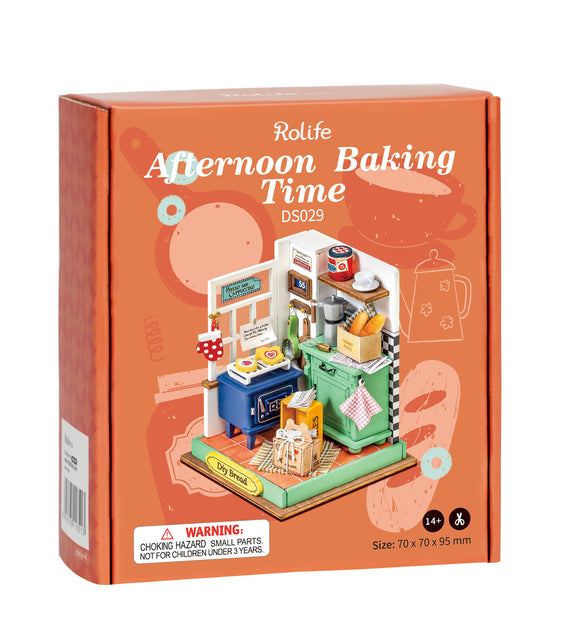 A detailed image of the Robotime DIY Afternoon Baking Time kit featuring a miniature kitchen setup. The kit includes a blue stove, green cabinets, baked goods, and kitchen utensils, all designed for crafting a charming baking scene.