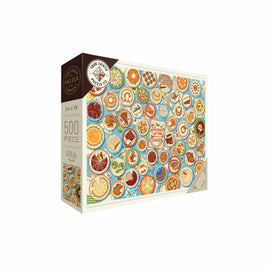 A colorful jigsaw puzzle box titled 'Desserts of the States' by True South Puzzles. The puzzle features various desserts illustrated on round plates against a blue background. There are 500 pieces, measuring 24x18 inches. The packaging showcases a variety of desserts from different states, highlighting regional specialties.
