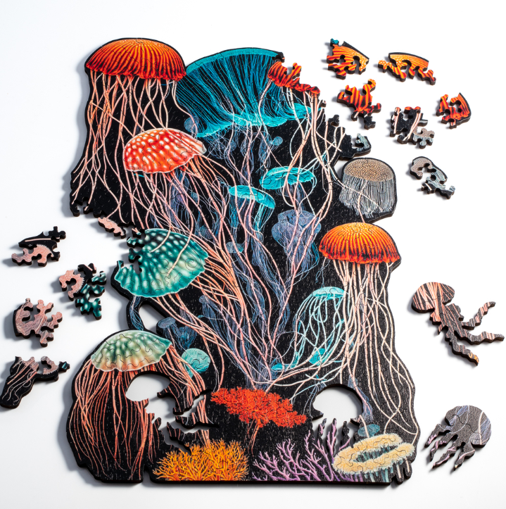 A colorful jigsaw puzzle titled 'Jellyfish Dreams' by Nervous System, depicting an underwater scene with several detailed jellyfish, vibrant coral, and intricate puzzle pieces scattered around. The jellyfish feature bright reds, blues, and greens, enhancing the ocean ambiance.