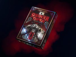The Stranger Things playing cards by Theory 11 feature a striking design with red and black accents. The box showcases iconic characters from the popular series, set against a mysterious background that captures the essence of the supernatural. Perfect for fans of the show, these cards combine nostalgia with quality craftsmanship for an engaging gaming experience.