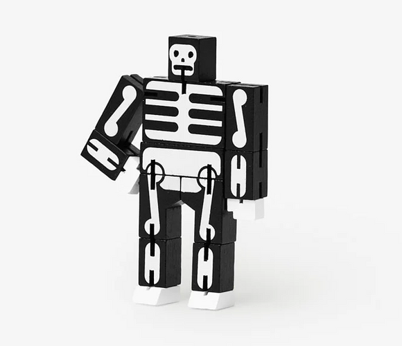 The Cubebot Micro Black Skeleton, a mechanical puzzle made by Harmony Ball, features a skeleton design with a black body and white bone details. The figure can be manipulated into different poses, showcasing its flexible joints.