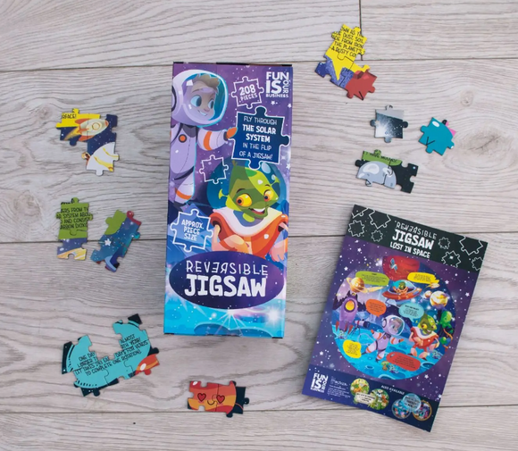 Outer Space Reversible Jigsaw puzzle by Boxer featuring vibrant illustrations of astronauts and aliens. The jigsaw includes 208 pieces with colorful designs to explore the solar system. The packaging and loose pieces are arranged on a wooden surface, showcasing the reversible aspect of the puzzle.