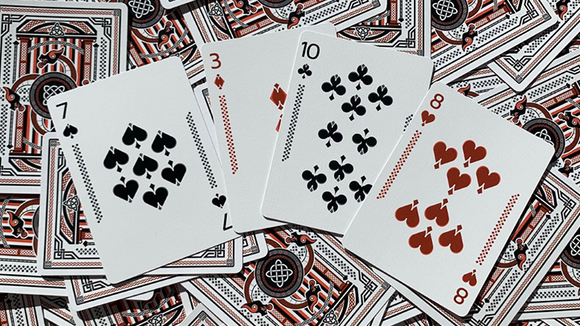 Close-up view of Vikings Bicycle Playing Cards featuring cards showing the numbers 7, 3, 10, and 8, each adorned with intricate designs and classic suits. The backdrop showcases additional cards, highlighting the vibrant colors and unique Viking theme.
