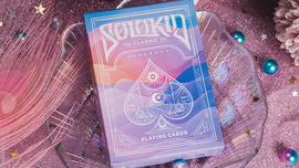 A beautifully designed deck of Solokid Rainbow Dream Playing Cards from Kings Wild. The box features an artistic blend of colors with a mystical card symbol on the front, set against a shimmering pink background, surrounded by decorative elements like stars and beads.