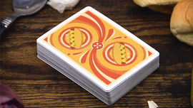 A deck of Hot Dog Playing Cards by Fast Food Playing Cards displayed on a wooden surface. The card back features a vibrant design with two illustrated hot dogs on a swirl pattern, surrounded by playful decorative elements. Nearby are some hot dog buns and a spoon, enhancing the fun food theme.