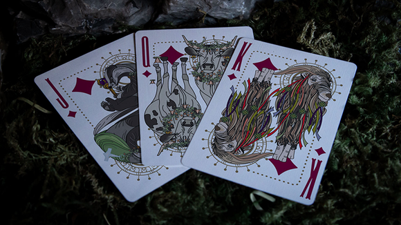 A close-up view of three Under the Moon playing cards by Jocu, featuring unique illustrations of animals adorned with floral crowns. The cards displayed are the Jack, Queen, and King, highlighted against a grassy background.