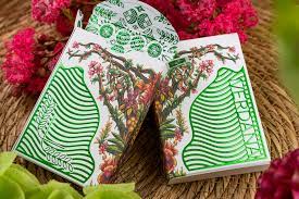 A close-up view of the Verdana Playing Cards from Legends Playing Card Co. The deck is beautifully designed with intricate floral patterns and vibrant green colors on the box, showcasing its artistic appeal. The cards are fanned open, displaying additional detailed illustrations on the backs, perfect for enthusiasts of card games.