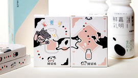 Pure Milk Playing Cards from Hanson Chien Production Co., featuring playful illustrations of cows and a character wearing a cow mask. The colorful packaging adds a whimsical touch to the card game.