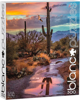 The Cactus Reflection jigsaw puzzle by Blanc Puzzles features a vibrant Arizona landscape with towering cacti and a picturesque sunset. The scene includes a winding dirt path reflecting the colorful sky and a soaring bird, capturing the serene beauty of the desert. This puzzle comes with 500 pieces, suitable for ages 14 and up.