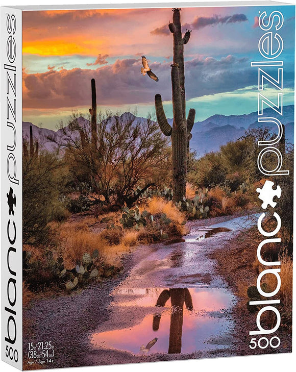 The Cactus Reflection jigsaw puzzle by Blanc Puzzles features a vibrant Arizona landscape with towering cacti and a picturesque sunset. The scene includes a winding dirt path reflecting the colorful sky and a soaring bird, capturing the serene beauty of the desert. This puzzle comes with 500 pieces, suitable for ages 14 and up.