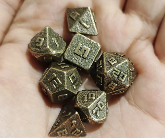 A close-up of a hand holding a set of 10MM ancient gold metal RPG dice. The dice feature engraved numbers with a textured surface, showcasing a classic and vintage design. There are multiple shapes including a d20, d12, d10, d8, d6, and d4, all in an ancient gold finish, ideal for role-playing games and tabletop adventures.