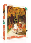 The Hollow jigsaw puzzle by New York Puzzle Company features a whimsical autumn scene with a girl on a bicycle adorned in a black skirt, striped stockings, and a green hat. She rides along a path lined with orange and yellow trees, carrying a pumpkin in her bike basket. The packaging showcases vibrant artwork and indicates it's a 500-piece puzzle, perfect for cozy indoor activities.