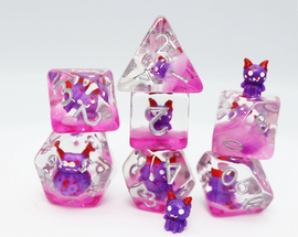 A vibrant Friendly Fiend RPG Dice Set featuring seven polyhedral dice made of translucent pink resin with purple and red detailing. The set includes a D4, D6, D8, D10, D12, D20, and a charming miniature figure of a friendly monster with purple and red accents. The dice are visually appealing with glitter suspended inside, perfect for tabletop gaming.