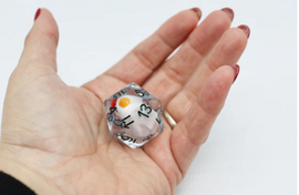 A person’s hand holding a 30mm Big Mama Hen D20 die. The transparent die features black numbers and a colorful orange dot, perfect for tabletop games and RPGs. The die's distinct size and design make it a standout choice for game enthusiasts.