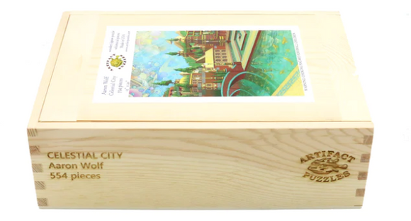 A wooden box packaging for the 'Celestial City' jigsaw puzzle created by Aaron Wolf. The box is elegantly crafted with the title and artist's name engraved on the side. A colorful image of a celestial cityscape is displayed on the top of the box, showcasing intricate details and vibrant colors. This jigsaw puzzle contains 554 pieces, ideal for puzzle enthusiasts and art lovers alike.
