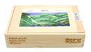 A wooden jigsaw puzzle box labeled 'Canaa Valley Angela Gomes' from Artifact Wooden Puzzles. The box features an illustration of a lush, green valley with rolling hills and vibrant purple flowers. It holds 148 puzzle pieces and has a warning label about choking hazards for small children.