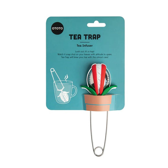 The Tea Trap Tea Infuser by OToto showcases a quirky design resembling a flower pot. The infuser features vibrant red flower petals, resting atop green leaves, with a metal infuser dome for brewing loose tea leaves. The packaging has playful graphics, including a cup of tea, and text featuring product details.