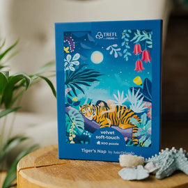 The Tiger's Nap Velvet Puzzle, created by Trefl, features a colorful illustration of a sleeping tiger surrounded by lush foliage, moonlight, and vibrant flowers. This high-quality 500-piece jigsaw puzzle is designed with a soft-touch velvet finish, making it perfect for puzzle enthusiasts and nature lovers alike.