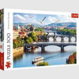 Trefl’s 500-piece jigsaw puzzle featuring a stunning view of Prague, Czech Republic. The image showcases the iconic Charles Bridge, lush greenery, and vibrant city architecture with a scenic river and boats, perfect for puzzle enthusiasts and lovers of travel art.