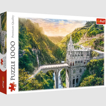 A 1000-piece jigsaw puzzle box featuring the Las Lajas Sanctuary in Colombia. The image showcases the stunning gothic-style church perched on a cliff with lush green mountains in the background, illuminated by a soft sunset glow.