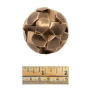 A spherical mechanical puzzle named Gob Stopper by Two Brass Monkeys, featuring interconnected geometric shapes in a bronze finish. The puzzle is displayed next to a ruler for size reference.