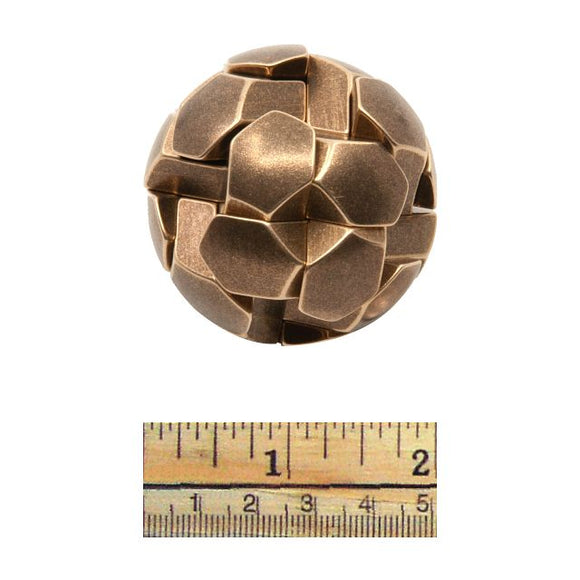 A spherical mechanical puzzle named Gob Stopper by Two Brass Monkeys, featuring interconnected geometric shapes in a bronze finish. The puzzle is displayed next to a ruler for size reference.