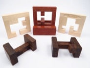 Portillon mechanical puzzle by Pelikan Puzzles featuring a collection of intricately designed wooden pieces in various shapes and sizes. The set includes a red, square-framed piece and two darker, rectangular shapes, showcasing craftsmanship and creativity. Ideal for puzzle enthusiasts seeking a challenging and engaging experience.