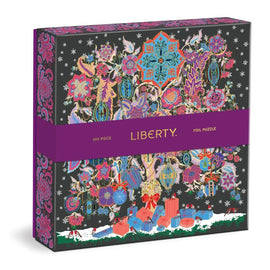 A beautifully illustrated box for the Christmas Tree of Life Foil Puzzle by Galison, featuring vibrant designs of ornaments, flowers, and gifts in rich colors against a dark background. The puzzle includes 500 pieces and showcases intricate foil detailing.
