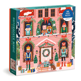 Colorful jigsaw puzzle box titled 'Nutcracker Magic' by Galison featuring a whimsical illustration of nutcrackers and holiday decorations. The box contains 500 pieces and showcases various festive characters in front of a pink house adorned with wreaths, lights, and gift boxes, perfect for holiday fun.