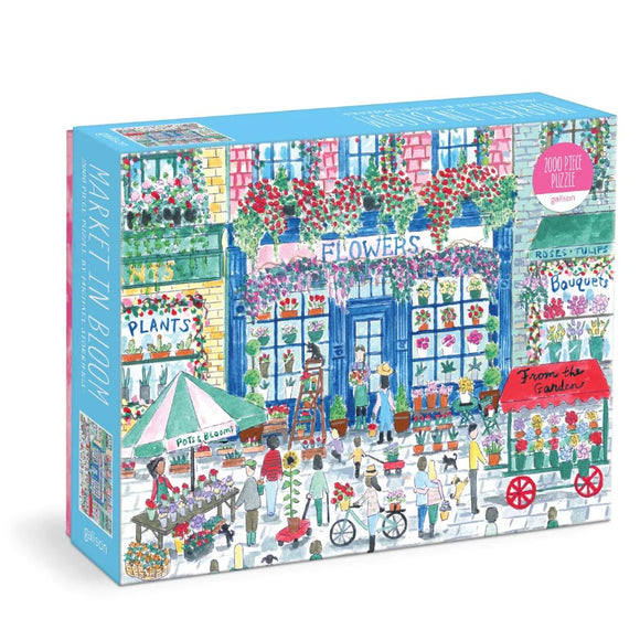 Michael Storrings Market in Bloom jigsaw puzzle by Galison, featuring a vibrant scene of a flower market with colorful stalls, people buying flowers, and a charming street lined with plants and bouquets. This 2000-piece puzzle captures the essence of a bustling open-air market, perfect for puzzle enthusiasts.