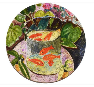 A round jigsaw puzzle depicting a colorful illustration of goldfish swimming in a glass bowl surrounded by green leaves and plants. The art style is reminiscent of Matisse, featuring vibrant hues and fluid lines that create a lively, tranquil scene.