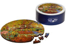 The Japanese Bridge in Monet's Garden jigsaw puzzle by Liberty Puzzles, featuring a vibrant, circular depiction of Monet's iconic bridge surrounded by colorful foliage. The puzzle pieces, displayed partially outside the round puzzle, exhibit intricate designs and colors that echo the original artwork, all housed in a stylish blue circular box.