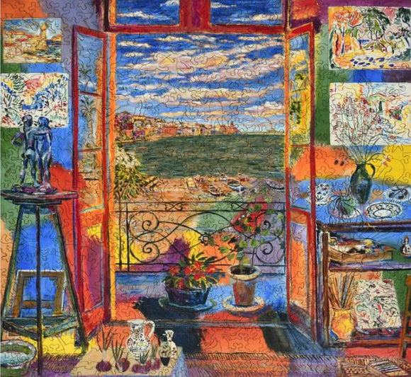 A colorful jigsaw puzzle depicting Matisse's studio, featuring an open window with a view of the sea and vibrant greenery. Inside the studio, various art pieces and sculptures are visible, with a table showcasing pottery and a potted plant.