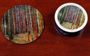 The Tannenwald jigsaw puzzle by Klimt features a vibrant forest scene with colorful trees. The puzzle pieces are displayed on a circular wooden table next to the round packaging, which showcases the same forest artwork. The puzzle's design is inspired by Gustav Klimt's artistic style, inviting puzzle enthusiasts to immerse themselves in a captivating DIY experience.