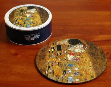 The Kiss round jigsaw puzzle by Liberty Puzzles, featuring an intricate design inspired by Gustav Klimt's famous artwork. The round puzzle is displayed beside its stylish cylindrical packaging, enhancing its aesthetic appeal and making it a perfect gift for puzzle enthusiasts and art lovers alike.