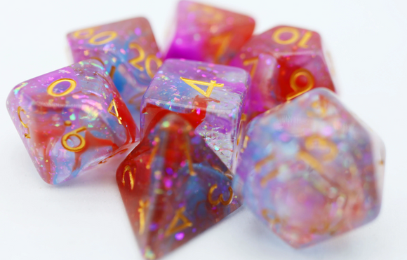 A vibrant set of Dawning RPG dice by Foam Brain, featuring colorful, translucent resin with iridescent sparkles. The 7-piece set includes various polyhedral shapes, each marked with luminous gold numbers, perfect for tabletop role-playing games.