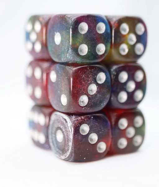Nebula Glitter 12 pc D6 Dice Set featuring vibrant, shimmering colors with a galaxy effect. The dice are semi-transparent with silver pips, stacked for display.