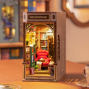 A beautifully crafted DIY Book Nook miniature by Robotime, featuring a cozy bookstore setup. The scene includes a bright red armchair, shelves filled with colorful books, and a small reading table. Soft lighting enhances the inviting atmosphere, while a sign indicates 'SHAKESPEARE' above the entrance. Perfect for book lovers and DIY enthusiasts.