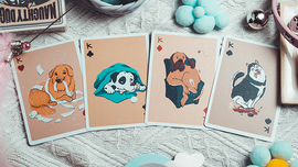 A playful display of Naughty Dog Playing Cards by 808 Magic and Bacon Playing Co. Featuring colorful illustrations of four dog characters on the King cards, showcasing their mischievous antics. The cards are arranged on a textured white fabric surface alongside playful decorative elements, capturing the fun spirit of the game.