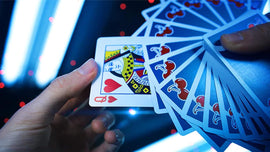 A hand holding a Cherry Casino Tahoe Blue playing card featuring a Queen of Hearts design, surrounded by a spread of other blue-backed cards. The scene is lit with ambient lights, creating a vibrant atmosphere suitable for gaming.