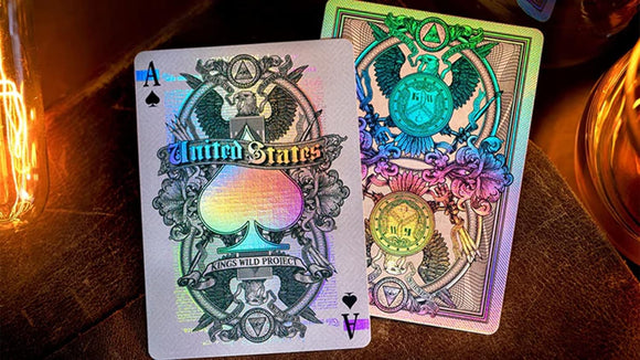 Two luxurious playing cards from the Legal Tender series by Kings Wild. The cards feature intricate designs with vibrant holographic elements, showcasing an Ace of Spades with the text 'United States' and ornate details such as eagles and geometric shapes.