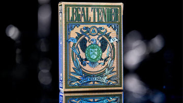 A beautifully designed deck of Legal Tender Luxury Playing Cards by Kings Wild. The box features intricate artwork with an emblem surrounded by elegant patterns, showcasing the number 13. The cards are presented against a reflective surface that enhances their luxurious appeal.