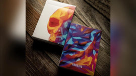 A vibrant and artistic depiction of the Memento Mori Genesis Playing Cards by Murphy's Magic, featuring an abstract design with geometric shapes and a colorful skull motif on the box. The front of the box showcases a striking blend of colors including orange, purple, and blue, making it visually appealing for card game enthusiasts.