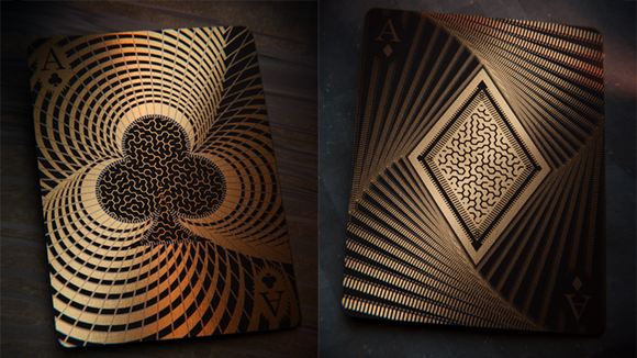 Chakravyuh (The Maze) Playing Cards featuring intricate designs on the backs of the cards. The Ace of Spades displays a swirling pattern with a black club symbol, while the Ace of Diamonds showcases a diamond shape enveloped in a maze-like design, both in gold and black colors, set against a dark background.