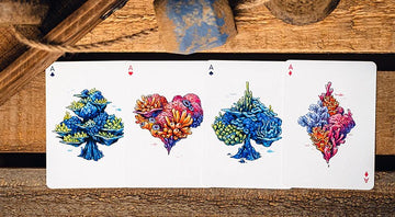 A close-up view of four beautifully illustrated playing cards from the False Anchors V4 (Deep Sea) deck. Each card features vibrant, colorful coral-inspired designs. The cards are arranged in a fan shape on a rustic wooden surface, surrounded by natural textures that enhance their aquatic theme.