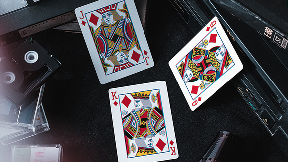 Colorful 3D playing cards with intricate designs featuring the King, Queen, and Jack of diamonds, laid out on a textured black surface surrounded by assorted game accessories. The cards showcase vivid colors and artistic illustrations, ideal for a fun game night.