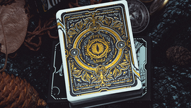 The Words of Dragon Playing Cards by King Star feature a beautifully designed back, showcasing intricate golden patterns and an eye motif, resting on a dark surface among natural elements like pine cones and dried leaves. This visually captivating deck is perfect for game enthusiasts and collectors.