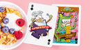 A vibrant display of Frost'd Playing Cards from Howlin' Jack's featuring whimsical designs. The Ace of Spades showcases a quirky character labeled 'Buffed & Puffed,' while another card highlights 'Trapper Snaps,' depicting a colorful scene with cartoon characters enjoying a meal. The cards are set against a pastel pink background with a bowl of cereal topped with blueberries and raspberries.